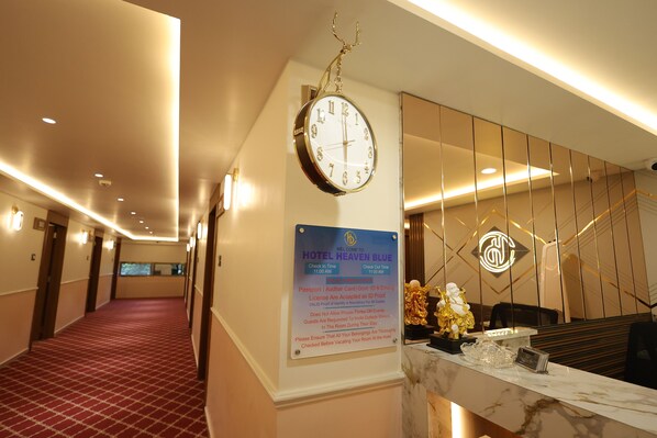 A hotel reception area with a clock, a welcome sign, and a check-in/out time sign. - Hotel Heaven Blue (Rajkot)