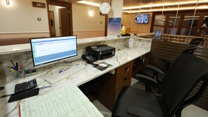 A hotel reception desk with a computer, phone, and various office supplies. - Hotel Heaven Blue (Rajkot)