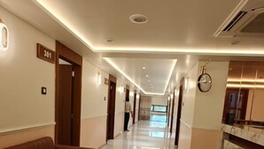 A hotel corridor with a brown sofa, a reception desk, and a clock on the wall. - Hotel Heaven Blue (Rajkot)