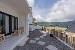 A balcony with a gravel floor, wooden furniture, and a view of a mountainous landscape. - Villa Dangka Kintamani Mitra RedDoorz (Bali)