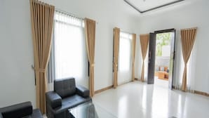 A spacious living room with a glass coffee table, black leather sofas, and beige curtains. - Villa Dangka Kintamani Mitra RedDoorz (Bali)