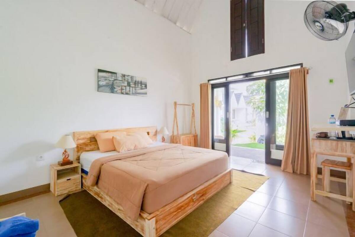 A bedroom with a bed, bedside table, and a view of the outdoors through a glass door.