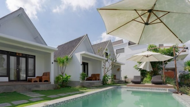 A modern pool area with a clear pool, lounge chairs, and umbrellas. - Villa Dangka Kintamani Mitra RedDoorz (Bali)