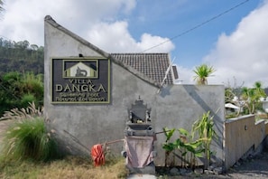 A concrete wall with a sign for Villa Dangka, a swimming pool, and a small shrine.