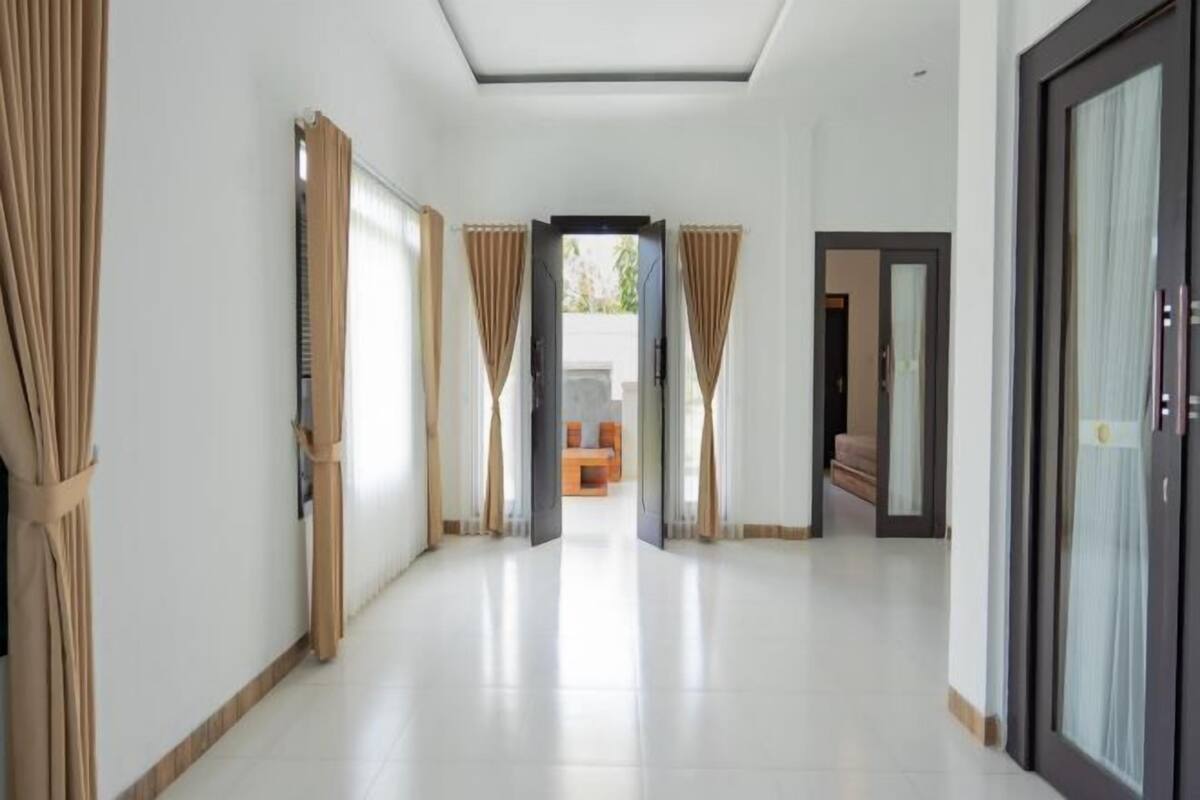 A hallway with a view to a seating area, a door leading to another room, and a window with curtains.