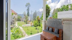 A room with a view of a garden, a wooden bench, and a white wall. - Villa Dangka Kintamani Mitra RedDoorz (Bali)