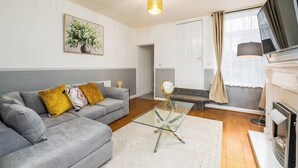 A living room with a grey sofa, a glass coffee table, a fireplace, and a television. - Modern 3 bed perfect for contractors and families (Maltby)