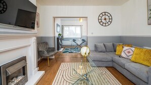 A modern living room with a fireplace, a sectional sofa, a glass coffee table, and a decorative globe. - Modern 3 bed perfect for contractors and families (Maltby)