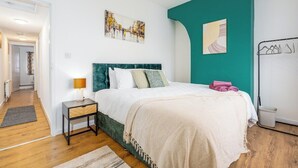 A bedroom with a bed, a nightstand, a lamp, a painting, and a wall-mounted drying rack. - Modern 3 bed perfect for contractors and families (Maltby)