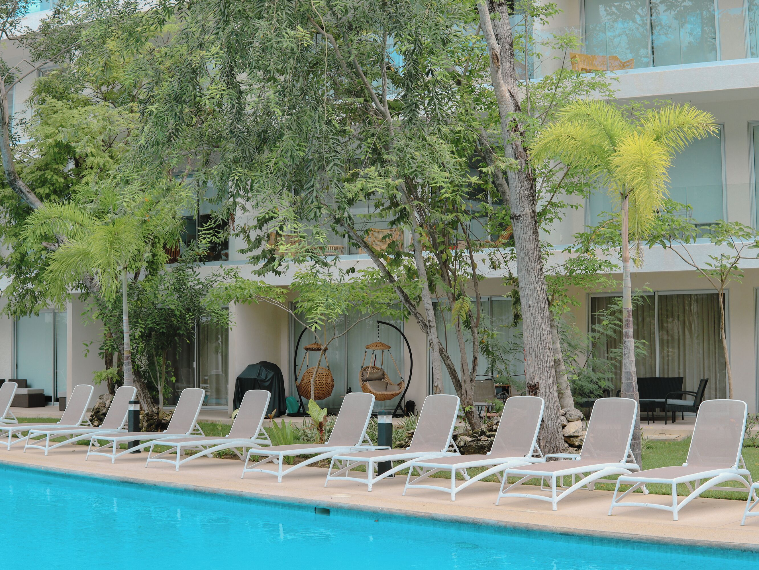 Un espace piscine avec des chaises longues et un bâtiment doté de grandes fenêtres et de balcons.