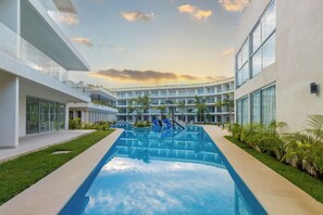 Un hotel moderno con piscina central, varios balcones y abundante vegetación.