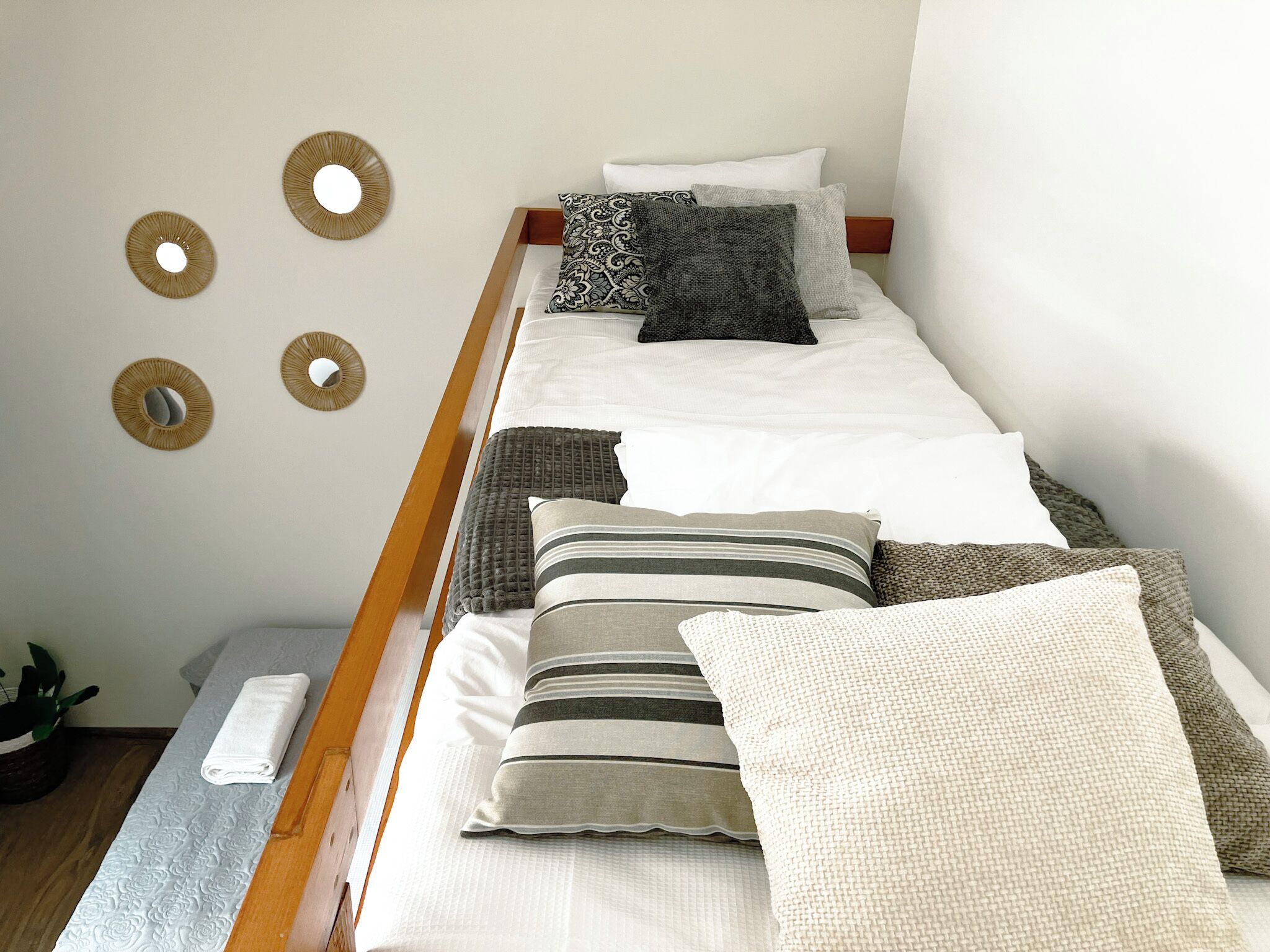 A single bed with a wooden frame, white bedding, and multiple pillows in various patterns and textures.
