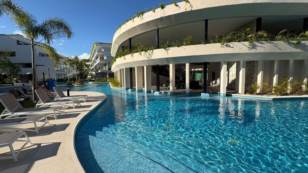 Ein modernes Hotel mit großem Schwimmbad, Liegestühlen und einem bogenförmigen Gebäude mit viel Grün.