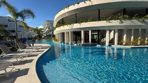 Un hotel moderno con una amplia piscina, sillas de descanso y un edificio curvo con vegetación.