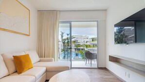 Ein modernes Hotelzimmer mit einer Couch, einem runden Holztisch, einem großen Fenster mit Blick auf einen Pool und Gebäude sowie einem an der Wand befestigten Fernseher.
