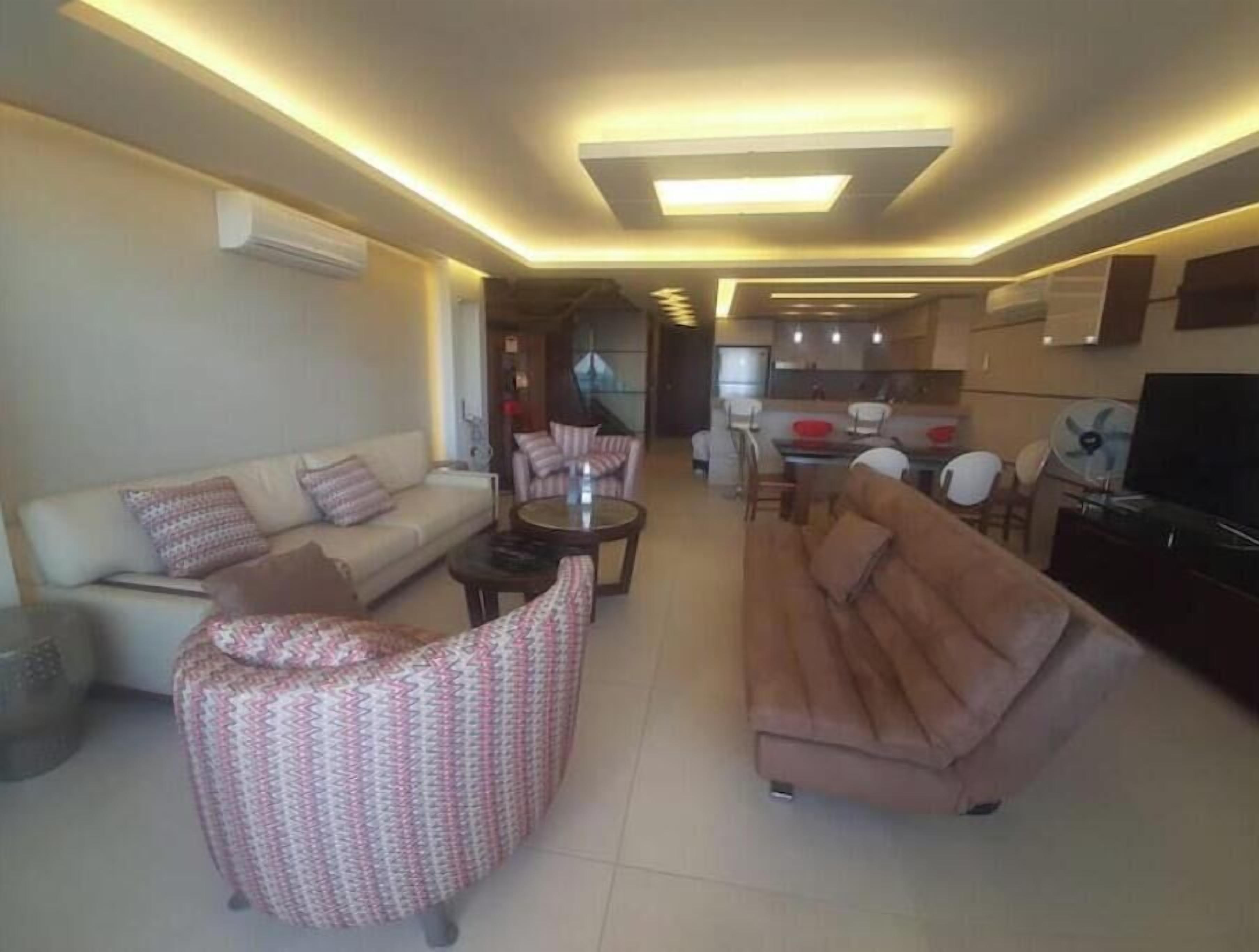A modern living room with a sofa, armchairs, a coffee table, and a TV.