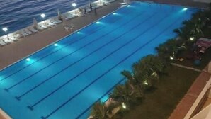 En swimmingpool med flere baner, omgivet af palmer og havudsigt i solnedgang.
