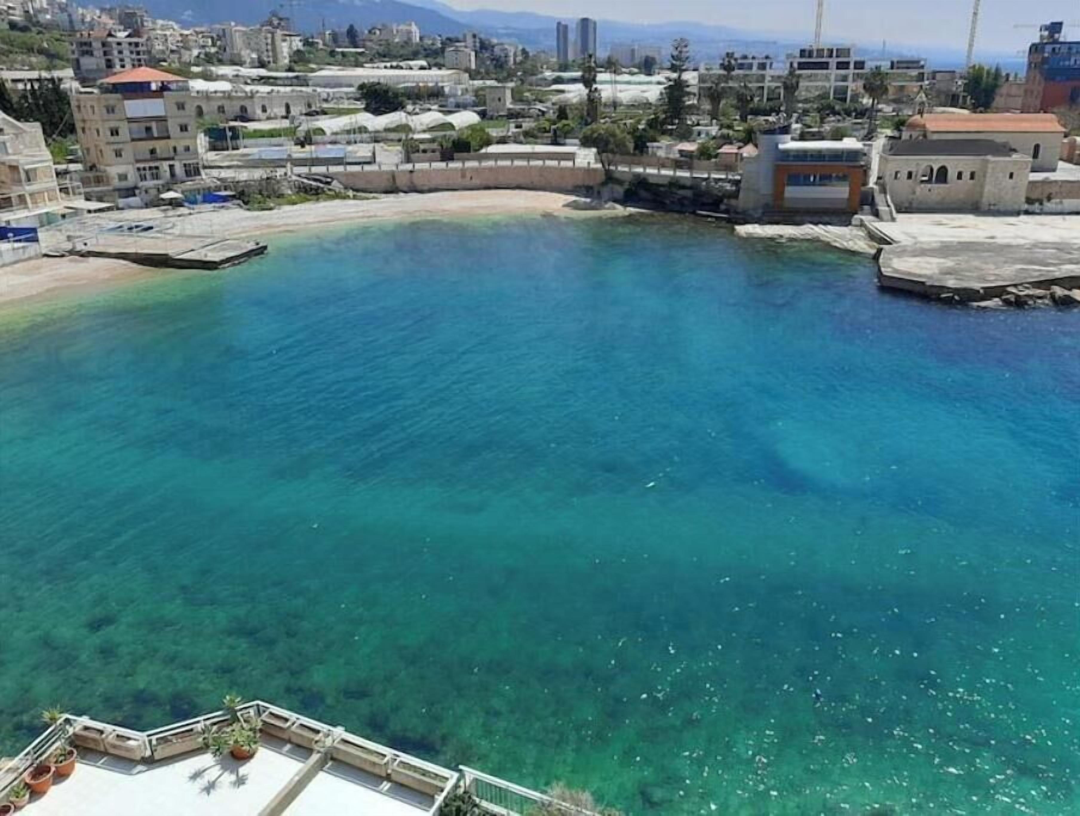 Una zona costera con aguas azules cristalinas, edificios y un paseo pavimentado.