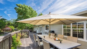 A wooden deck with a table and chairs, a large umbrella, and a house in the background.
