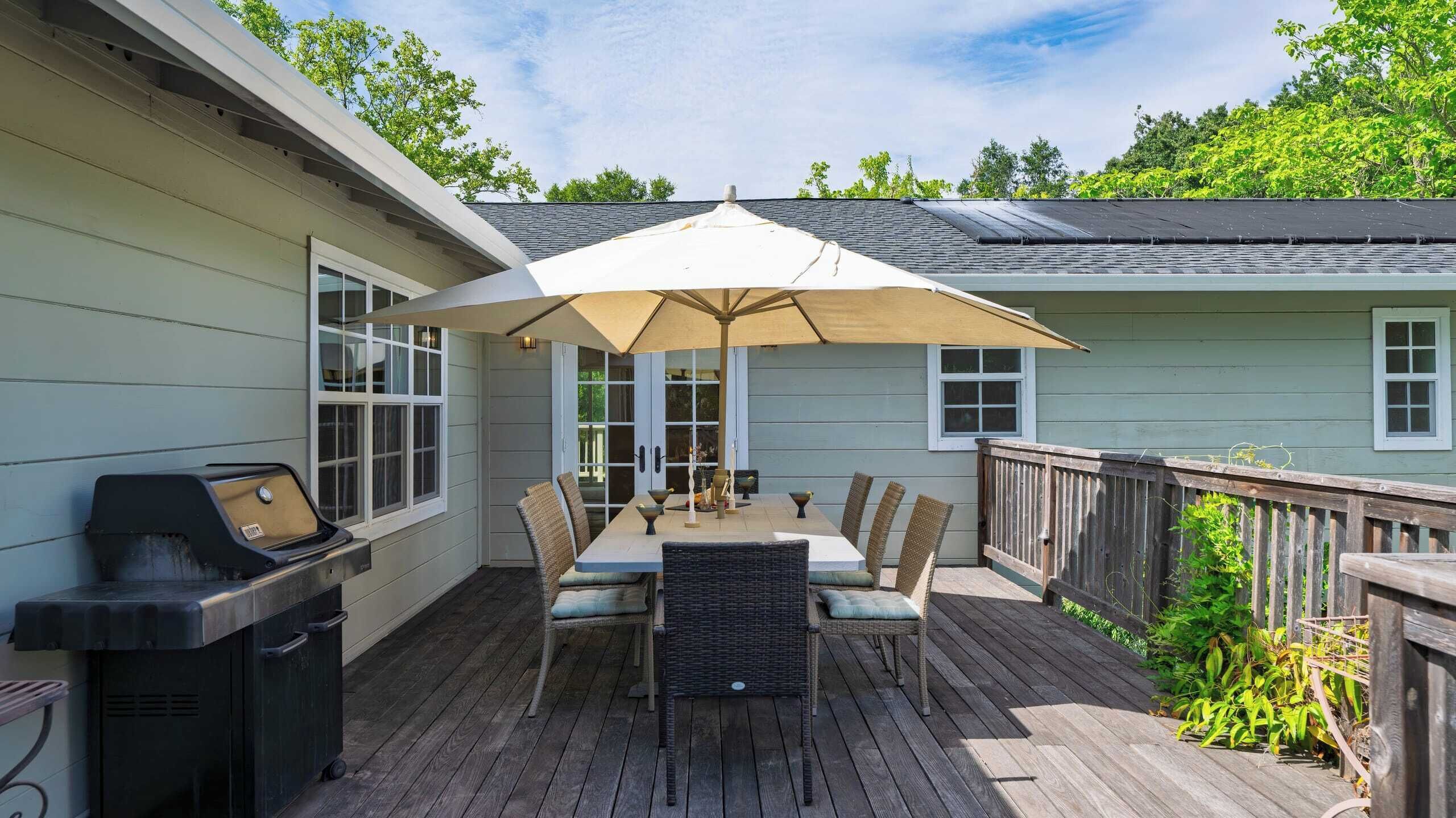 A covered patio with a table and chairs, a grill, and a wooden deck.