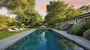A swimming pool with lounge chairs, a hammock, and a house with a staircase.