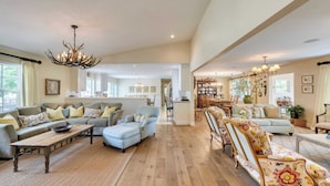 A spacious living room with a wooden floor, a sofa set, a dining area, and a chandelier.