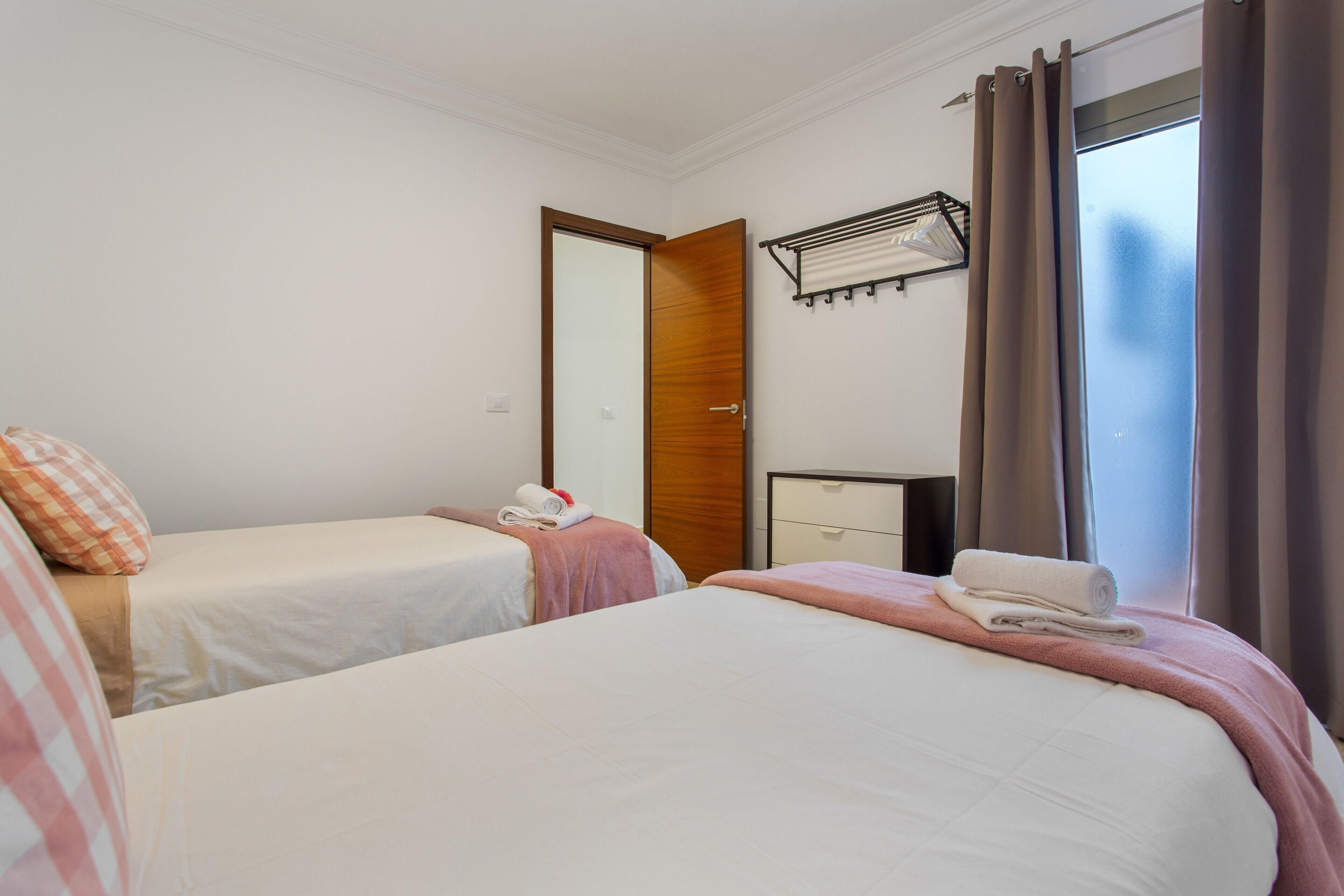 Una habitación de hotel con dos camas, una puerta de madera, un escritorio pequeño y una ventana con cortinas.