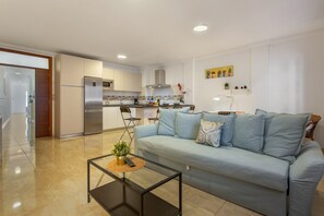 Una cocina moderna con refrigerador, microondas y estufa. Hay un sofá azul claro con almohadones decorativos y una mesa de centro de vidrio con una planta.