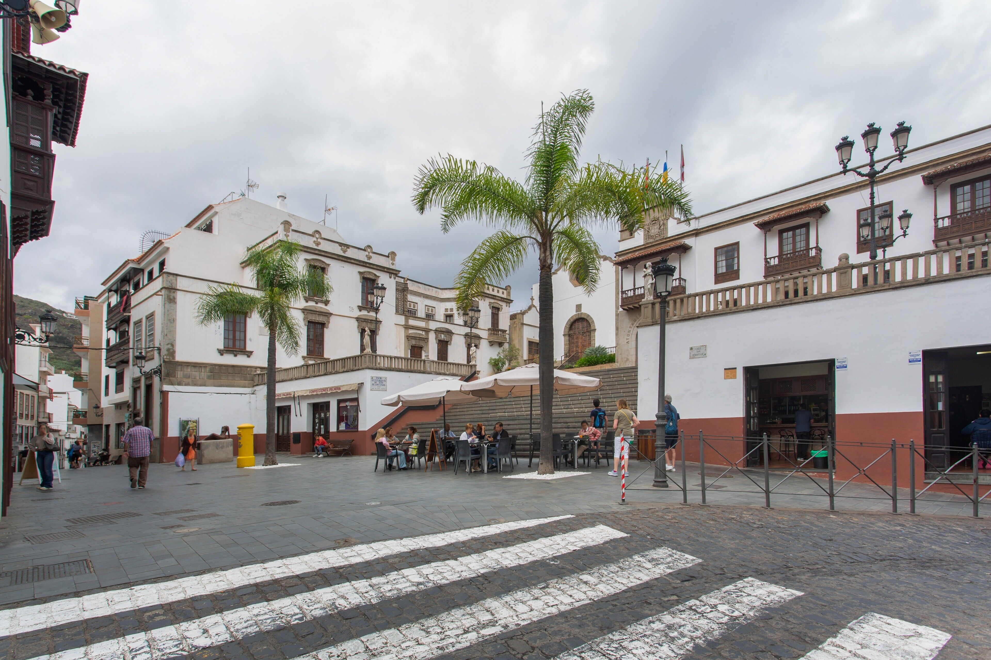A plaza with buildings, palm trees, and outdoor seating areas.