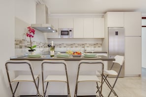 A modern kitchen with white cabinets, a stainless steel refrigerator, a microwave, and a dining area with four chairs.