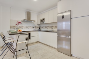 A modern kitchen with white cabinets, a stainless steel refrigerator, a microwave, and a sink.