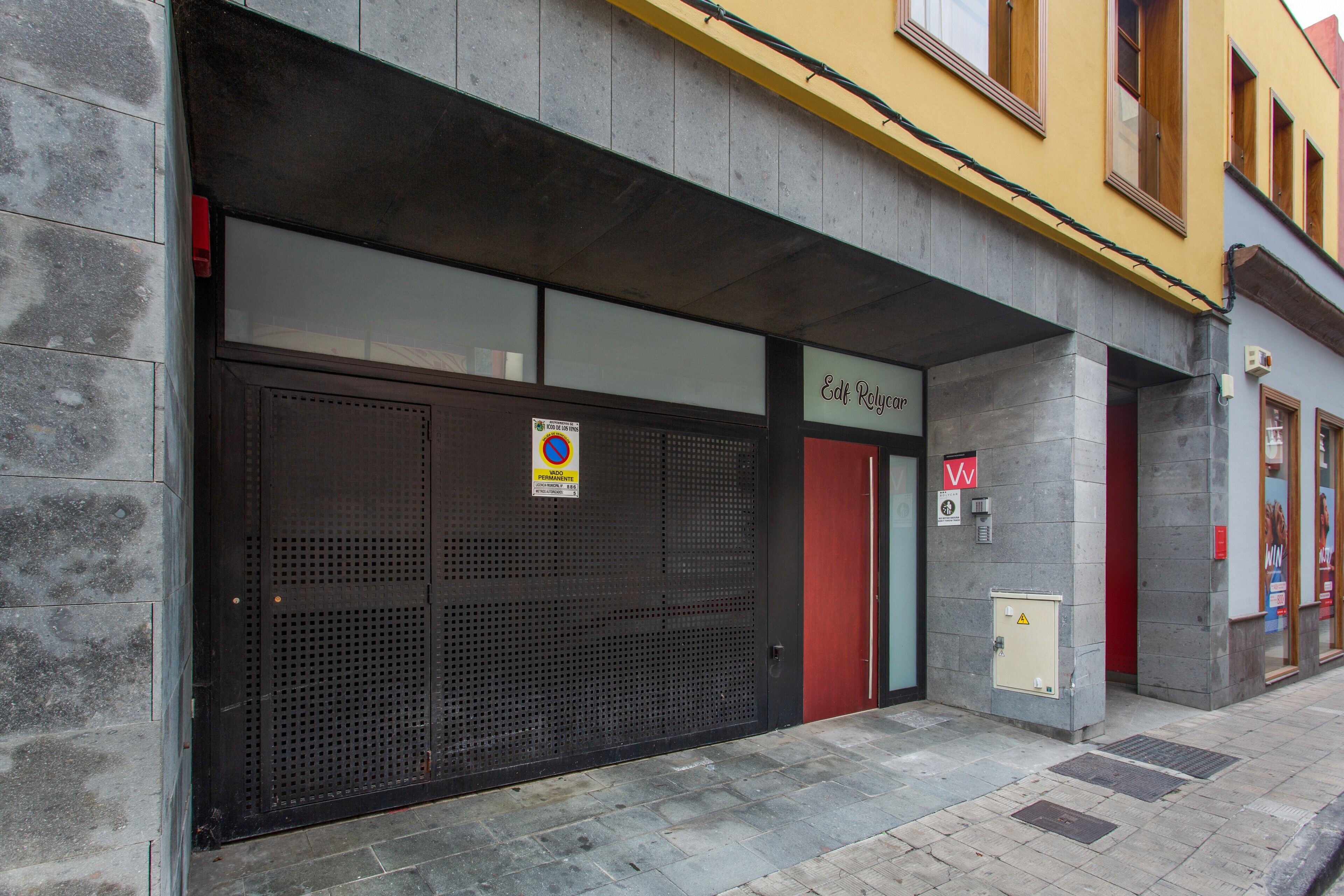 A building with a closed metal shutter door, a red door, and a sign with a yellow background.