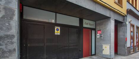 A building with a closed metal shutter door, a red door, and a sign with a yellow background.