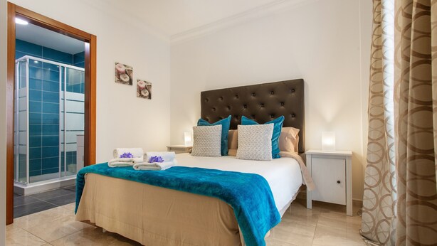 Ein Schlafzimmer mit einem großen Bett, einem Nachttisch, einem Badezimmer mit Glasdusche und einer Tür zum Balkon.