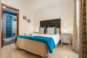 Une chambre dotée d’un grand lit, d’une table de chevet et d’une salle de bain avec une douche en verre, ainsi que d’une porte donnant sur un balcon.