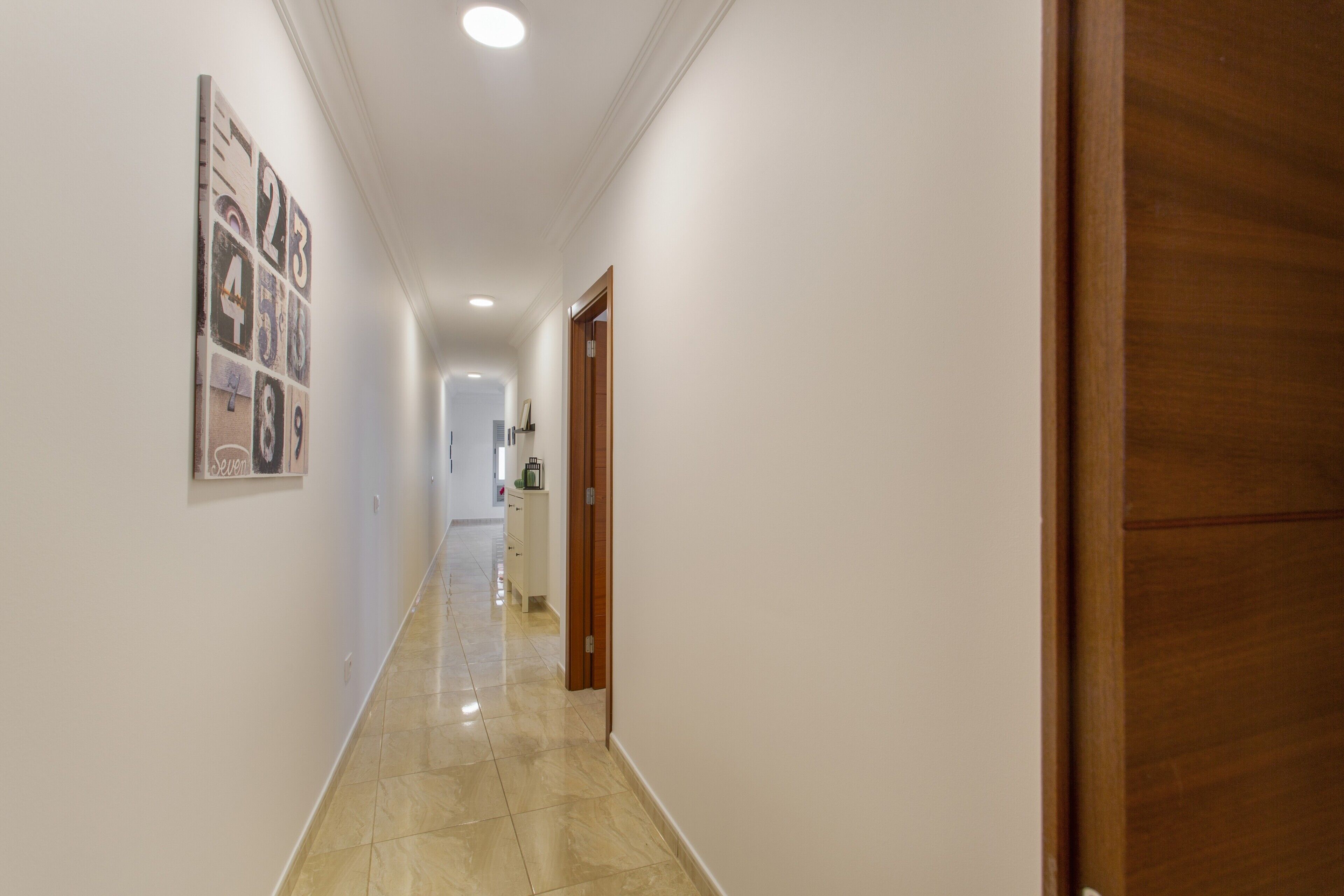 Un corridoio con una porta in legno, un muro bianco e un pavimento piastrellato.
