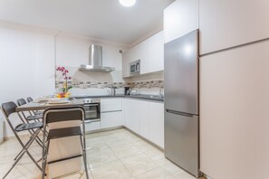 Una cocina moderna con gabinetes blancos, un refrigerador de acero inoxidable, un microondas y una zona de comedor con sillas y una mesa.