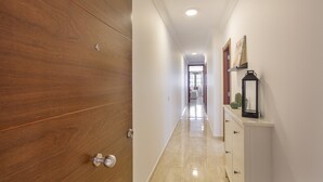 Un couloir avec une porte en bois, un mur blanc, une armoire blanche avec un miroir et un sol carrelé.