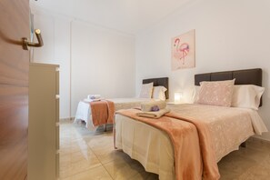Habitación de hotel con dos camas, una puerta de madera, una pared blanca y un cuadro de un flamenco.