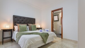 A neatly made bed with a tufted headboard, two bedside tables with lamps, and a bathroom visible through an open door. - Holiday Apartment 'Rolycar 204' with Wi-Fi (Icod de los Vinos)