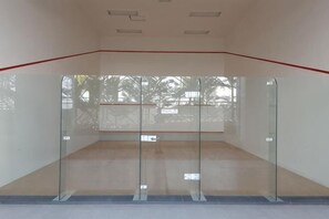 A squash court with glass walls, a red line marking the playing area, and a visible exit sign.