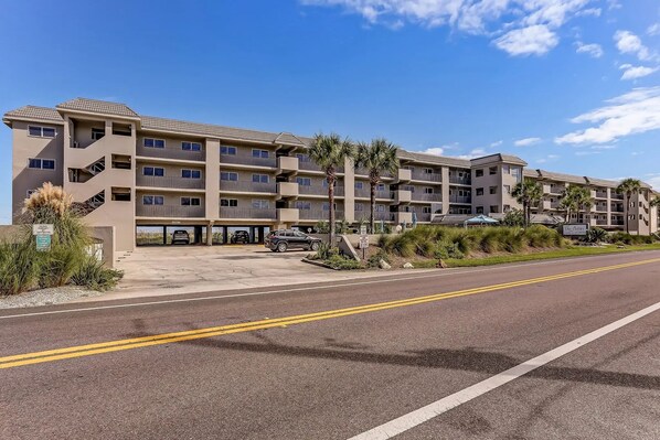 A multi-story hotel with a parking lot, palm trees, and a clear sky.