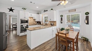 A modern kitchen with white cabinets, a central island, and a dining area with wooden chairs. - Austin's Hill Country Escape & Retreat – Private Oasis With Pool & Spa on Acre+ (Austin)