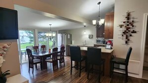 A modern kitchen with a dining area, wooden flooring, and a view of the outdoors.