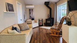 A cozy living room with a wooden floor, a ceiling fan, a fireplace, a television, and a comfortable seating area.