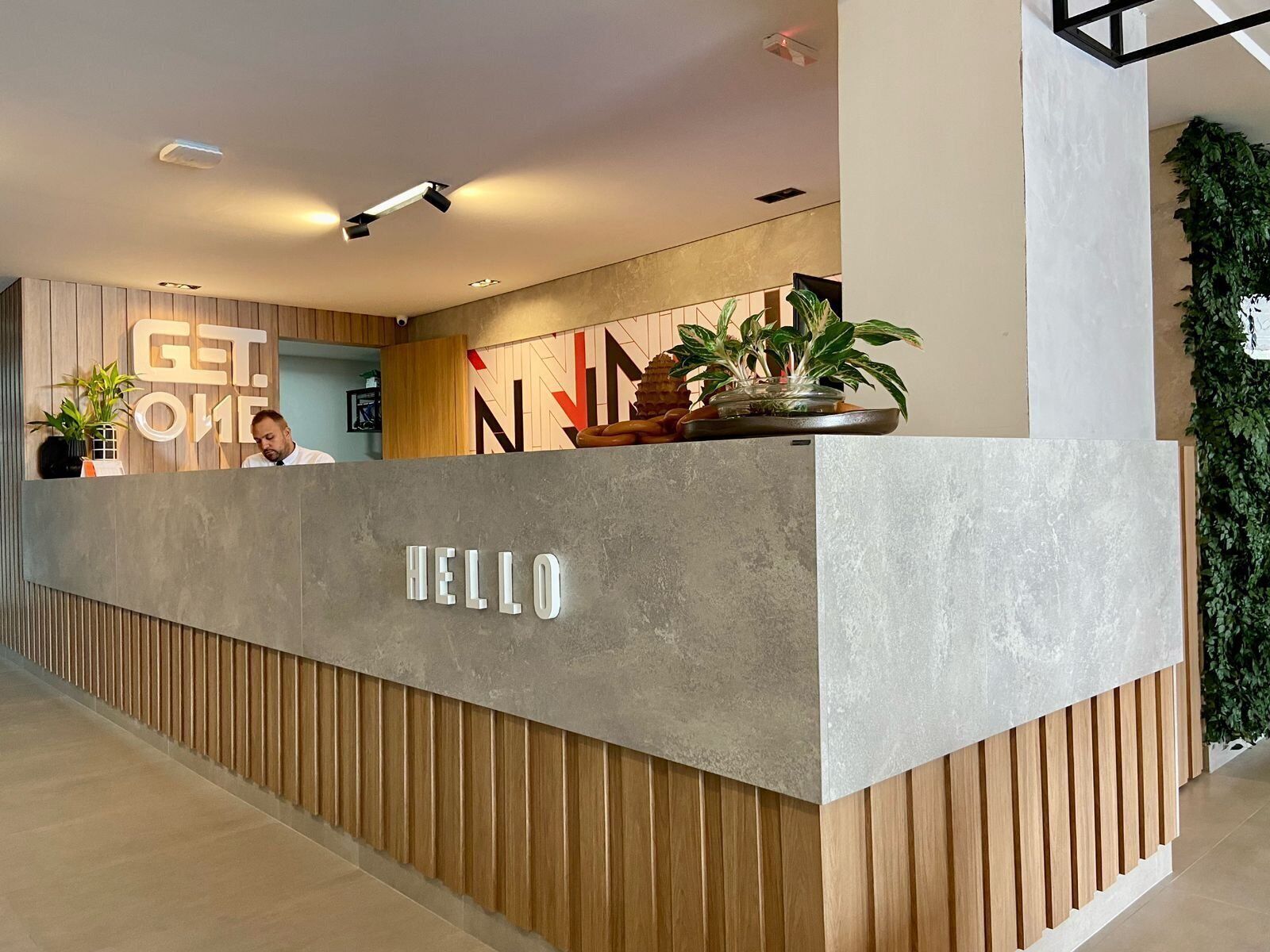 A reception desk with 'HELLO' signage, wooden paneling, and a potted plant.