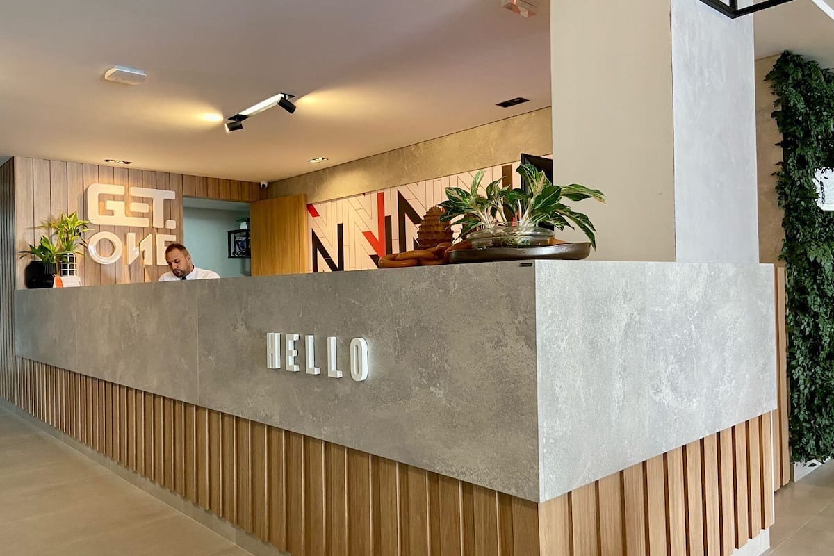 A reception desk with 'HELLO' signage, wooden paneling, and a potted plant.