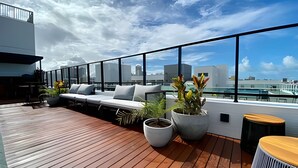 Une terrasse sur le toit avec une plateforme en bois, des sièges blancs rembourrés, des plantes en pot et une vue sur le paysage urbain.