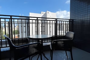 A balcony with two chairs and a table, a black railing, and a view of buildings. - Get One  (João Pessoa)