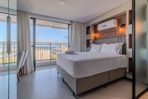 A modern hotel room with a large bed, a balcony with a view, and a built-in air conditioning unit. - Get One  (João Pessoa)
